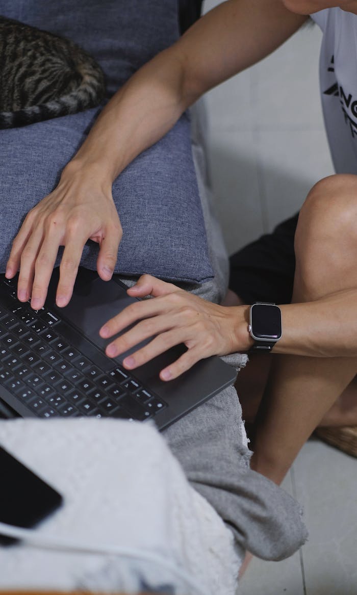 Close-up of a man typing on a laptop with a smartwatch, seated indoors, showcasing modern technology and lifestyle.