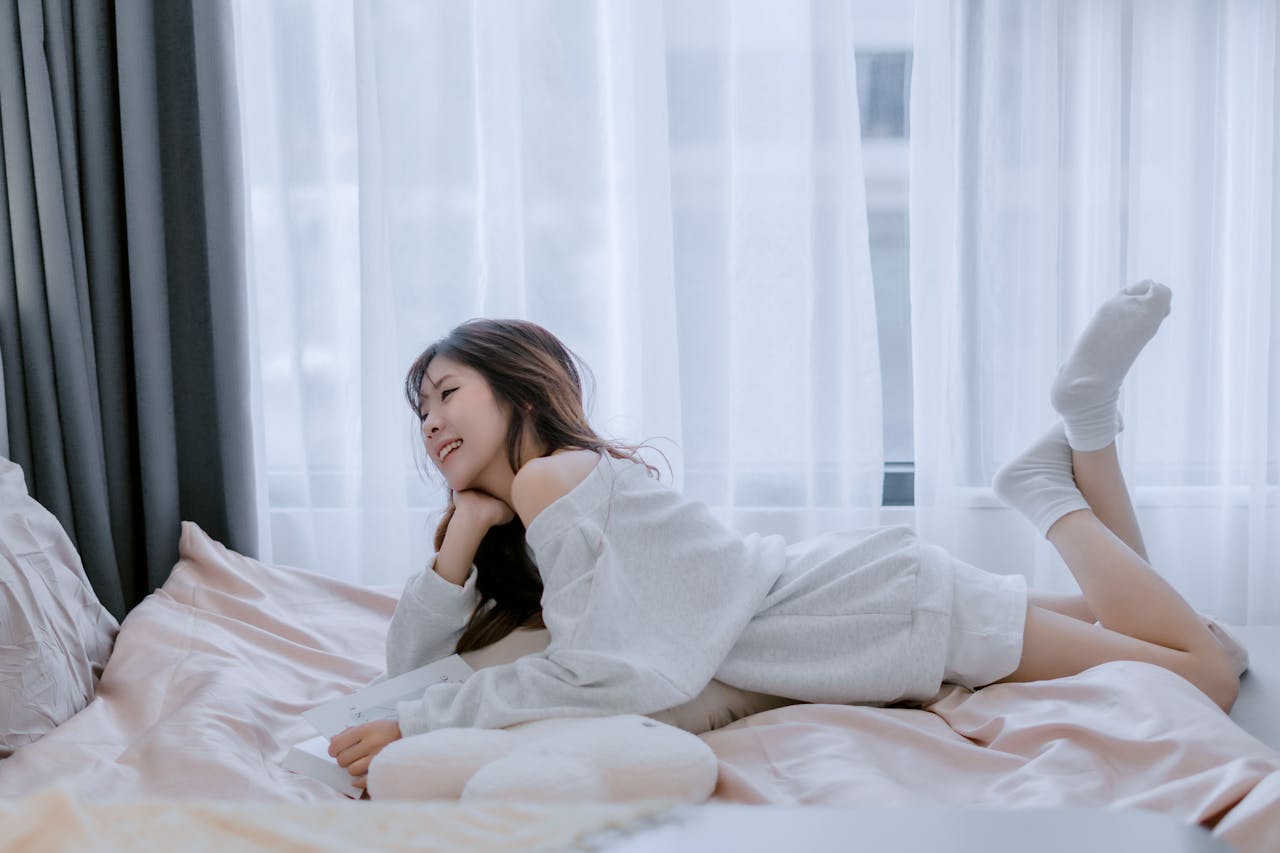 Young woman relaxing on a bed in a bright, cozy room, exuding comfort and serenity.