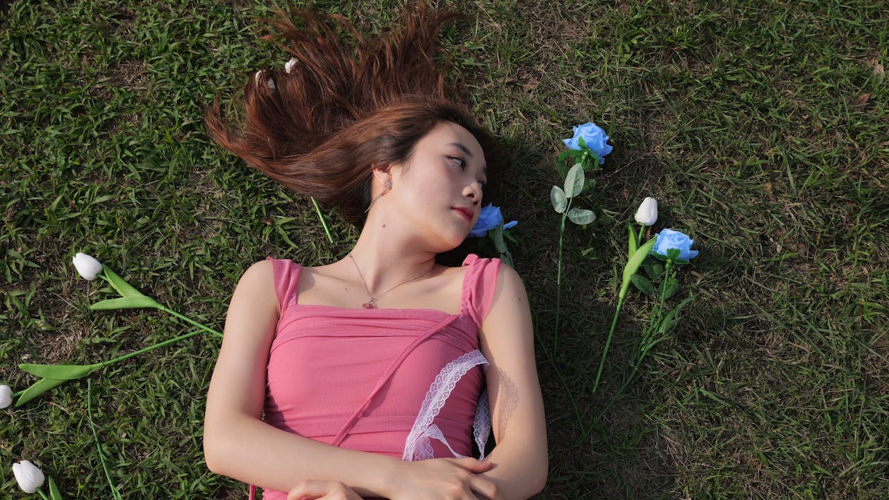 Young woman in pink dress lying on grass surrounded by blue and white flowers.