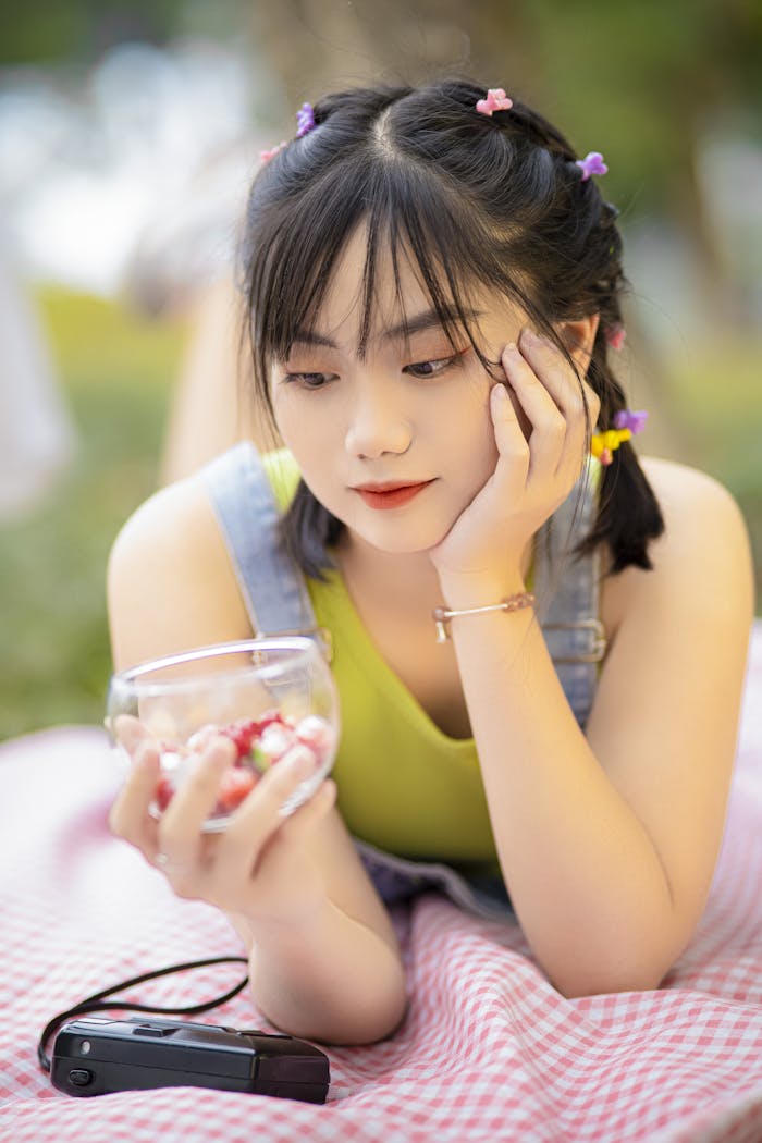 An adult woman enjoying strawberries at a picnic on a sunny day, showcasing relaxation and leisure.